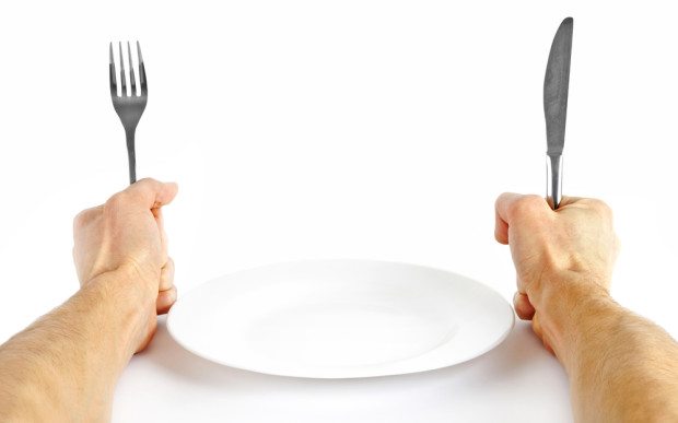 person holding a knife and fork in front of an empty plate