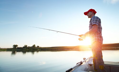 Young man fishing on a lake from the boat at sunset