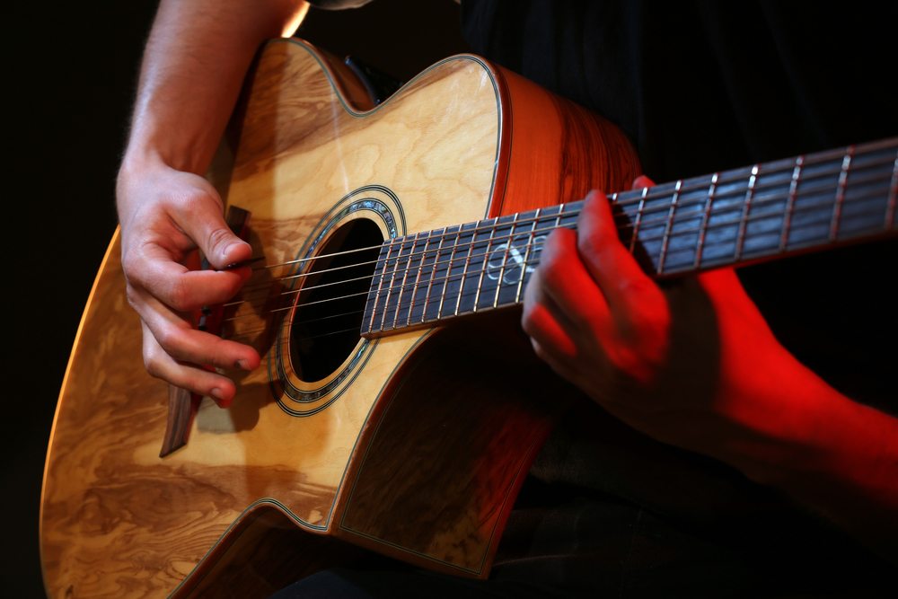Young man playing on acoustic guitar close up