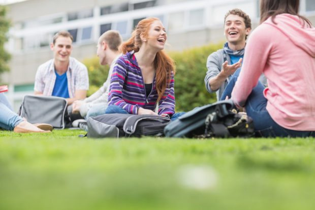 college students sitting outside with school supplies, laughing