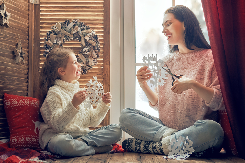 Mother and daughter making paper snowflakes by a window