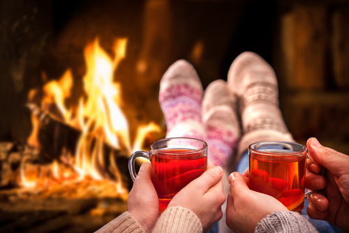 Couple wearing winter socks, drinking cider in clear mugs next to a fireplace