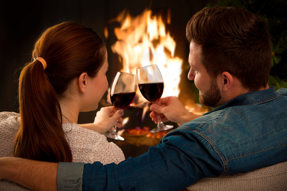 Couple relaxing with glass of wine at romantic fireplace on winter evening.