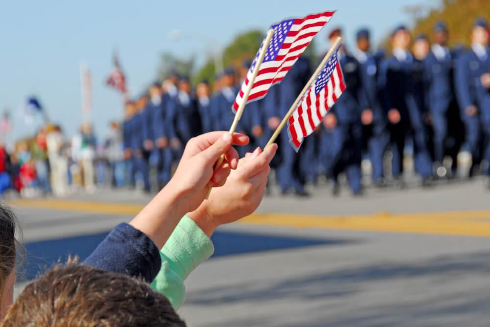 Photo of Kids Waving Little Flags during a Veterans Day Parade. Click Here to Learn about our Veterans Day Specials.