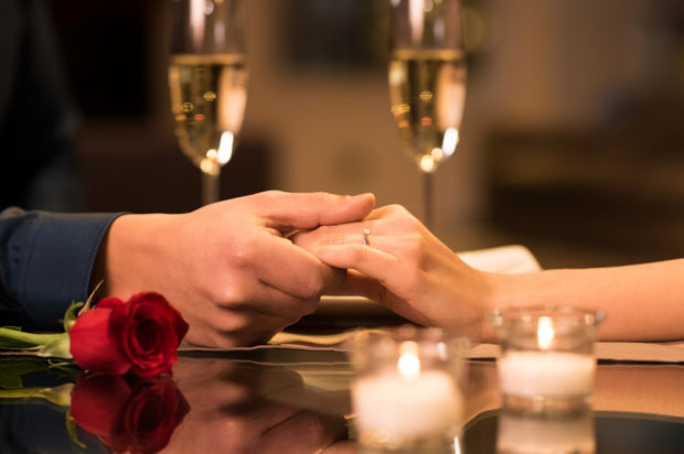 close up of couple holding hands with candles, a rose and champagne glasses